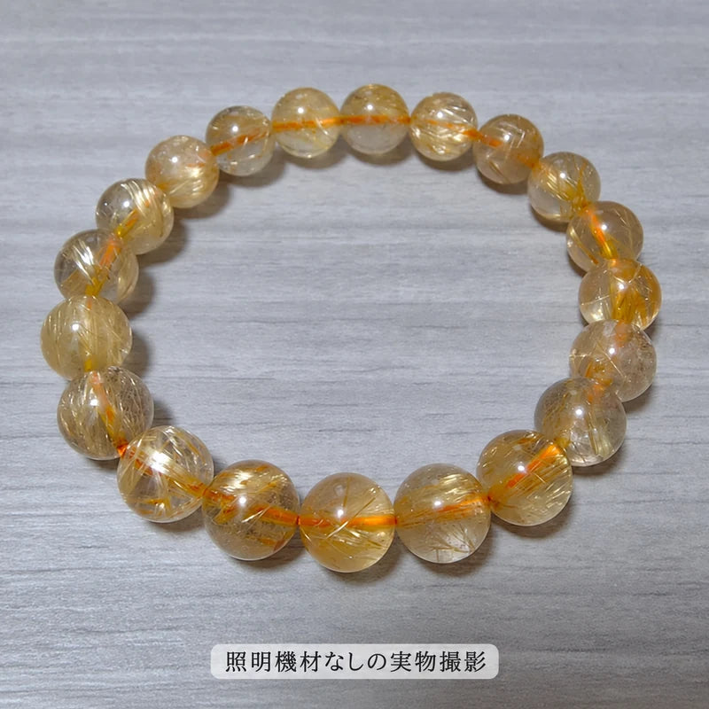 照明機材を使わずに撮影した、木目の台に置いたゴールドルチルブレスレットの全体写真