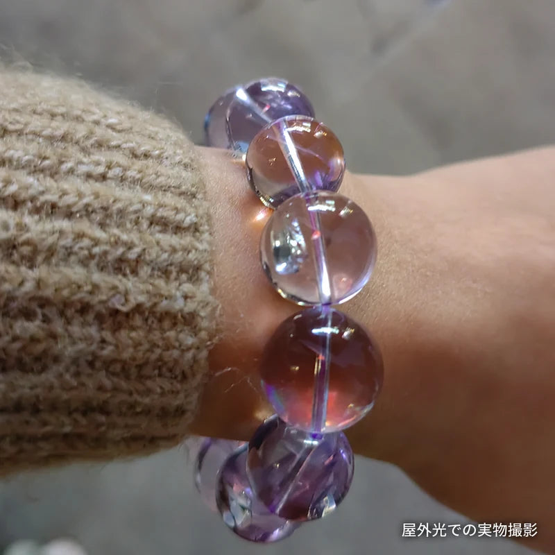 ベージュのニットの袖口に着けたボリビアアメジストブレスレットの接写。屋外光で丸玉の透明感を写した実物写真