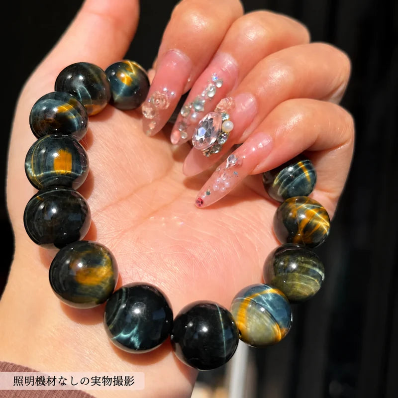 撮影用照明を使わずに撮影した、手のひらに載せた黒や青、金色の縞模様が見えるタイガーアイの丸玉ブレスレット