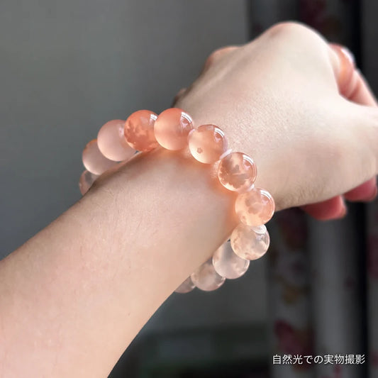 手首に着けた桜瑪瑙ブレスレットの横からの実物写真。自然光に透ける淡いピーチカラーの丸玉が見える