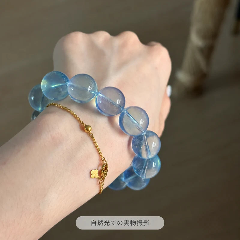 ゴールドカラーのチェーンブレスレットと重ね着けしたサンタマリアアクアマリンブレスレット。自然光の下で大粒の青い丸玉と透明感が見える実物写真