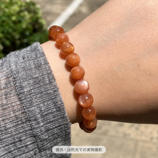 屋外の自然光で撮影した、グレーの袖口に合わせて手首に着けたサンストーンブレスレット