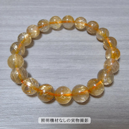 照明機材を使わずに撮影した、木目の台に置いたゴールドルチルブレスレットの全体写真