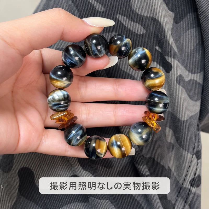撮影用照明を使わずに撮影した、黒や青灰色、金色の縞模様と琥珀色の飾りが見えるタイガーアイブレスレット