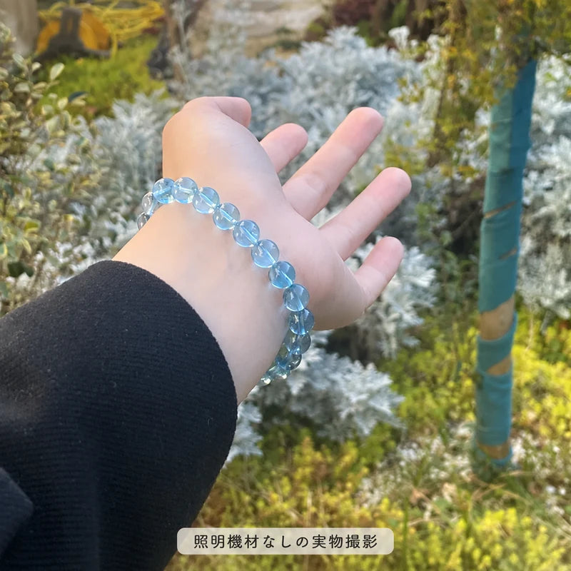 照明機材を使わずに屋外で撮影した、緑の植物を背景に手首に着けたブルートパーズブレスレットの写真