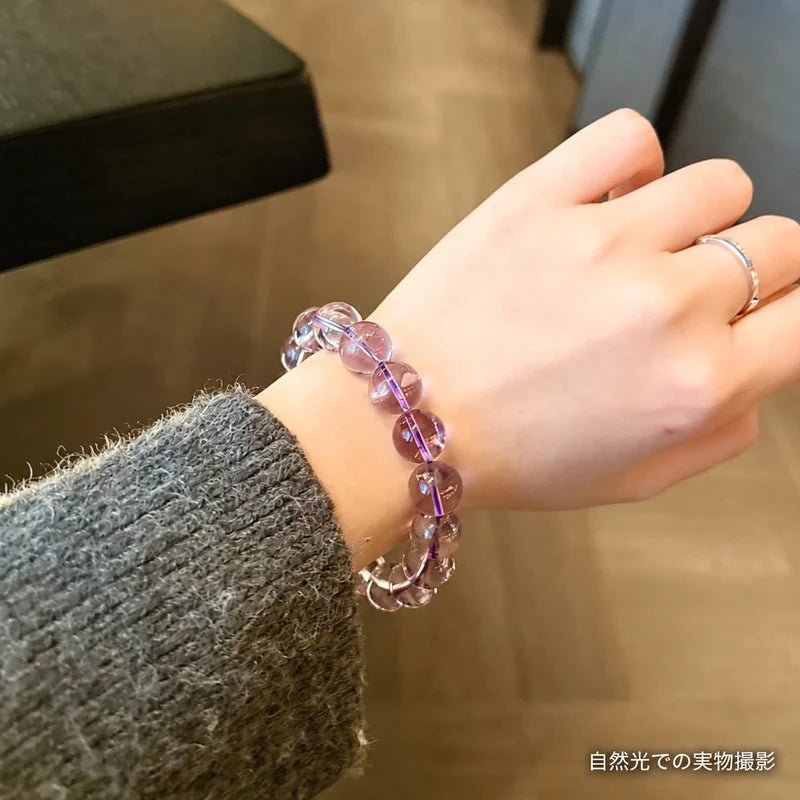 グレーのニットに合わせたボリビアアメジストブレスレット。自然光で淡い紫色の丸玉を写した着用写真
