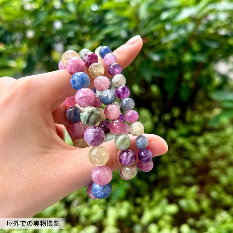 屋外で撮影した、指に複数本掛けた色とりどりのキャンディカラーエメラルドブレスレット