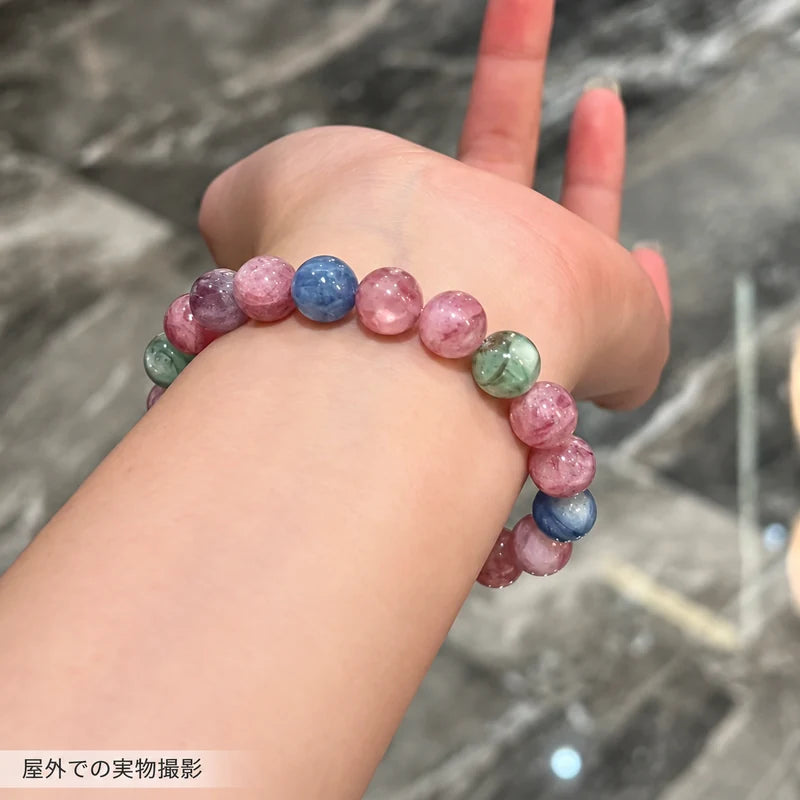 屋外で撮影した、手首に着けたキャンディカラーエメラルドブレスレットのピンクや青の丸玉が見える写真