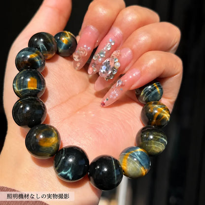 撮影用照明を使わずに撮影した、手のひらに載せた黒や青、金色の縞模様が見えるタイガーアイの丸玉ブレスレット