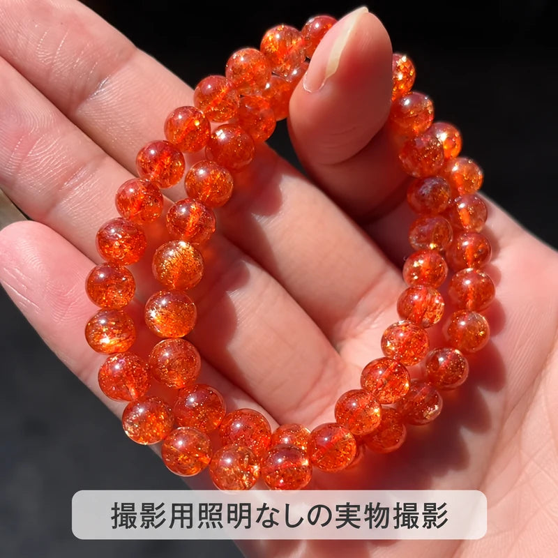 撮影用照明を使わずに撮影した、手のひらに掛けたオレンジ色の丸玉ブレスレットと内部のきらめきが見える写真