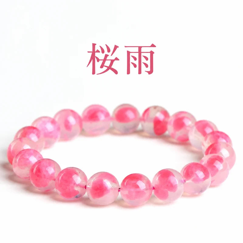 白い背景に置いた、花びらのようなピンクの模様が見える「桜雨」の丸玉ブレスレット