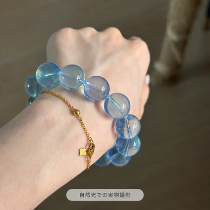ゴールドカラーのチェーンブレスレットと重ね着けしたサンタマリアアクアマリンブレスレット。自然光の下で大粒の青い丸玉と透明感が見える実物写真
