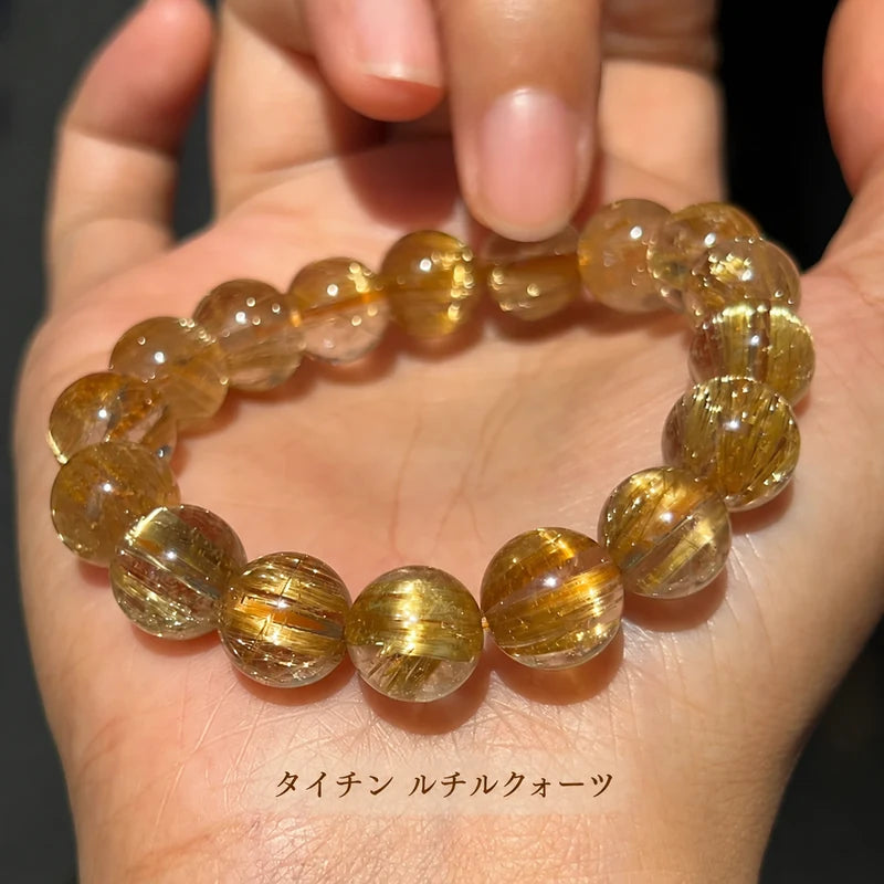 タイチンルチルクォーツの丸玉ブレスレット。手のひらに載せた透明な珠の中に、太い金色のルチルと細い針状の模様が見える
