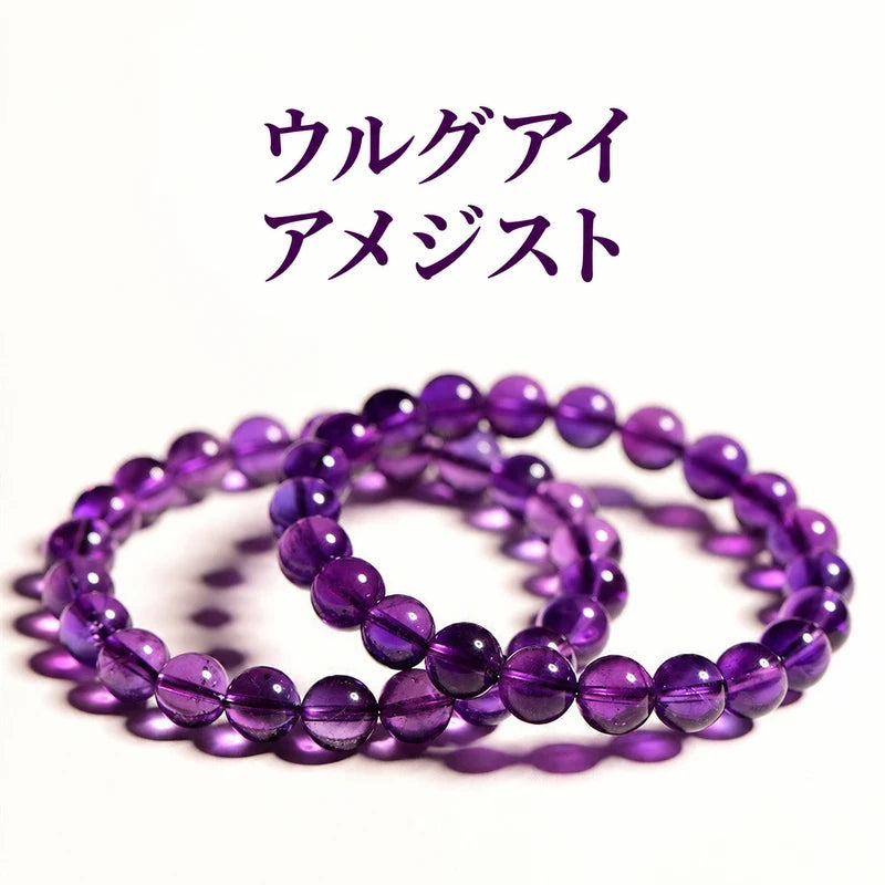 白い背景に重ねて置いたウルグアイアメジストの丸玉ブレスレット。深い紫色の珠と透ける光が見える