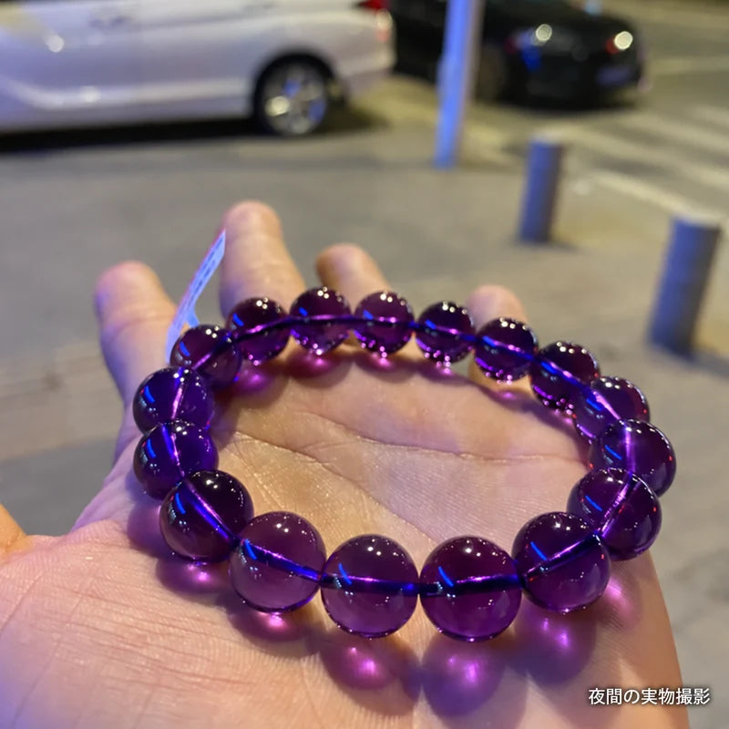 夜の街で手のひらに載せたウルグアイアメジストブレスレット。街灯の光が映る濃い紫色の丸玉を写した実物写真